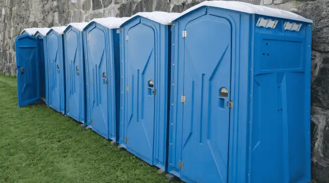 Row of blue portable toilets lined up on grass against a stone wall for event sanitation in Yonkers, NY