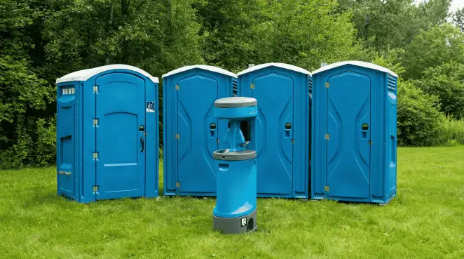 Four blue portable toilets and a matching hand washing station on grass near trees, a common sight at local outdoor events in Yonkers, NY