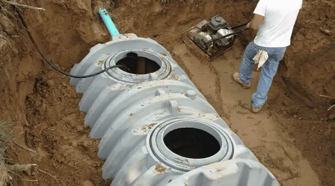 Septic tank installation showing a technician compacting soil around a new poly septic tank in an excavation pit in Yonkers, NY